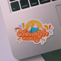 Orange and blue camping sticker that says Adventure Awaits. Includes a mountain range and camping tent