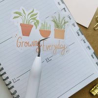 growing everyday potted plants clear sticker. 3 potted plants lined up with the phrase "growing everyday" below it written in hand lettered font