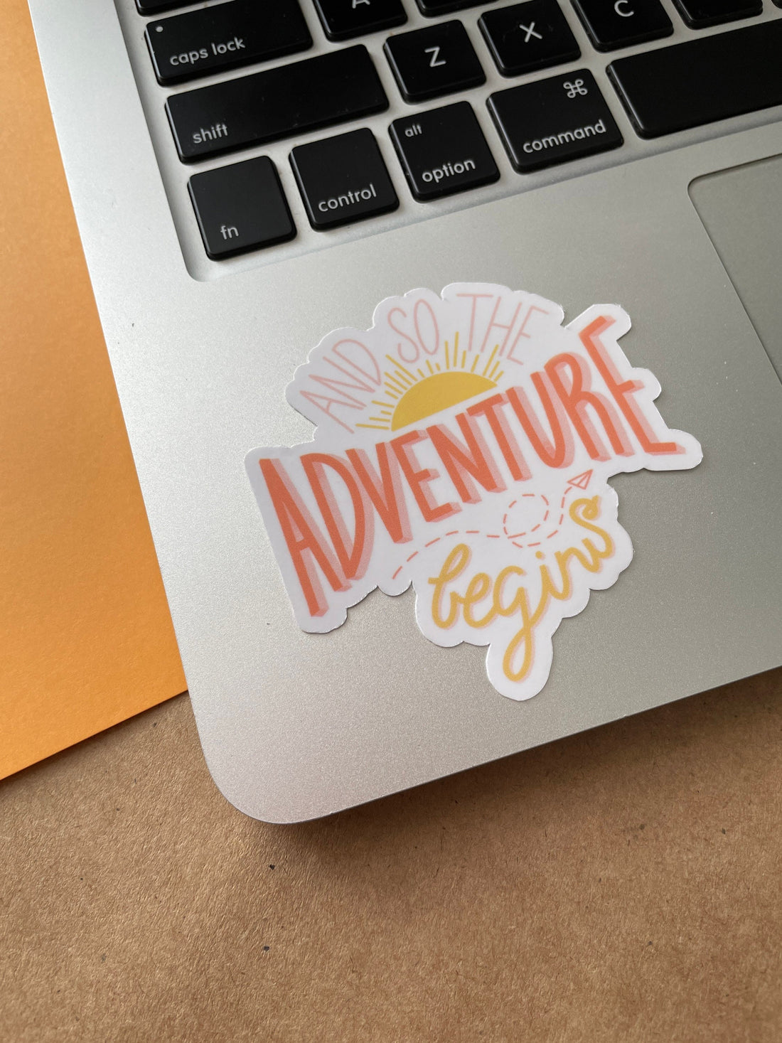 And so the adventure begins glossy vinyl sticker. A hand drawn sticker with sun rising and paper airplane. Sticker is on Macbook laptop bottom left near the keyboard