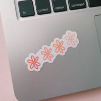 4 pink flowers vinyl sticker, that change in shade. Starting with the darkest on the left and lightest on the right. Sticker is on Macbook near keyboard