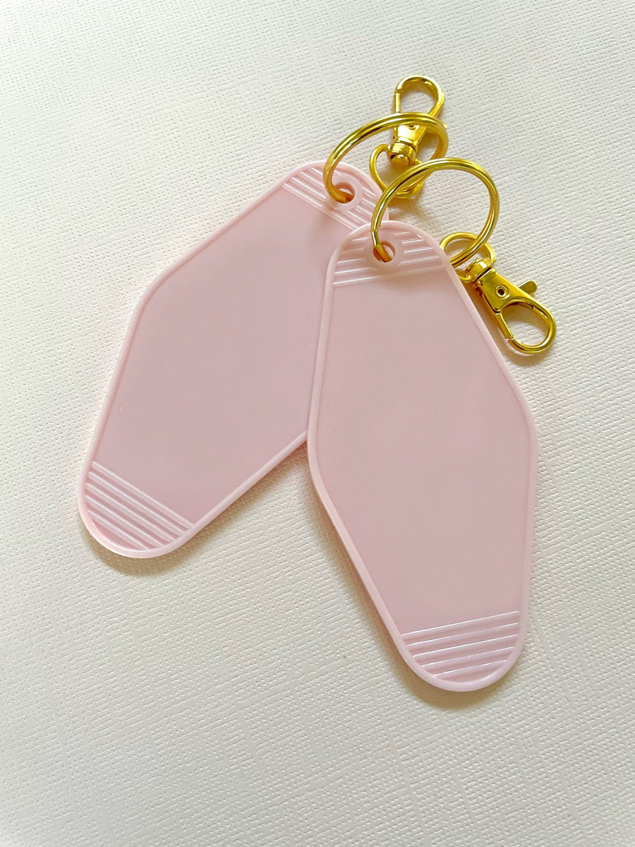 two blank hotel keychains in light pink. Both with gold keyring and lobster clasp