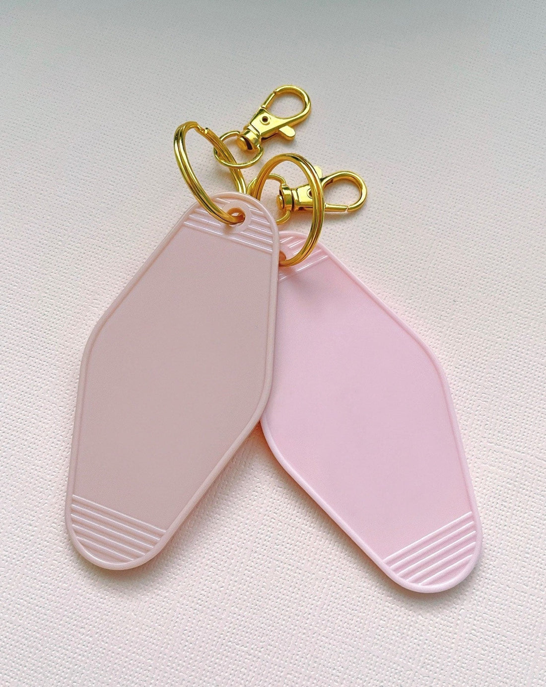 two blank hotel keychains, one beige and one light pink. Both with gold keyring and lobster clasp