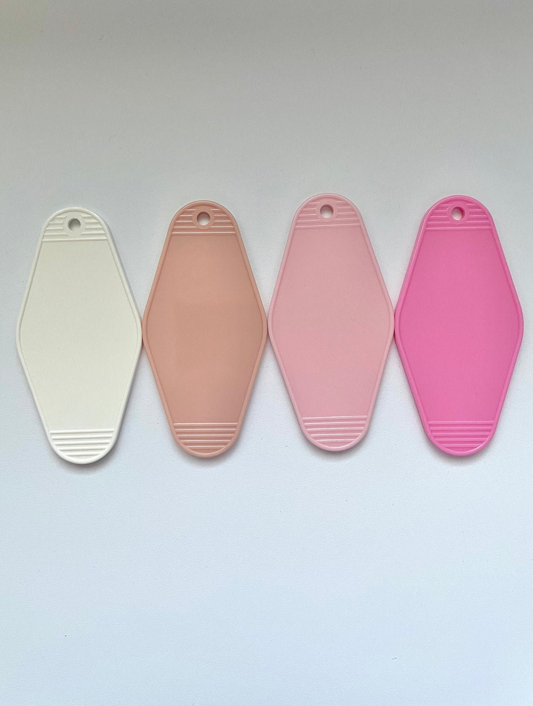 four blank hotel keychains for customization, one beige, one light pink, one white, and one bright pink