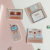 90s nostalgia collection full sticker pack, 4 fun stickers. A mixtape, floppy disk, zokia cell phone, and a polaroid camera that is all 90s themed